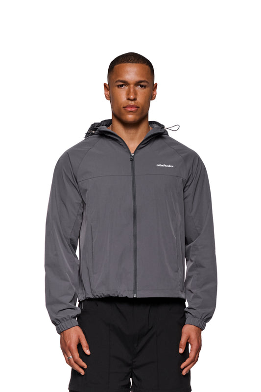 Mann trägt Windbreaker Dark Gray mit Reißverschluss, verstellbarer Kapuze und elastischen Bündchen. OLAKALA-Logo sichtbar.