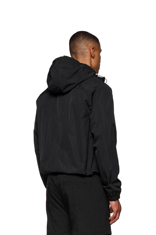 Mann trägt Windbreaker Black mit verstellbarer Kapuze und Reißverschlusstaschen, ideal für Wind- und Wetterschutz. OLAKALA-Stickerei auf der Brust sichtbar.