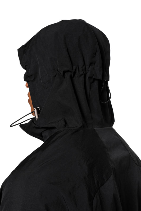 Person trägt Windbreaker Black mit verstellbarer Kapuze, Reißverschlusstaschen und OLAKALA-Stickerei. Wind- und wasserdicht, unisex Design, reguläre Passform.