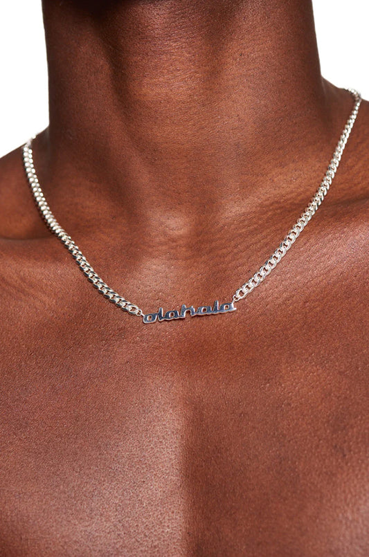 Person trägt die CC Logo Chain Silver Halskette mit OLA KALA Anhänger und 0,5 cm breiter Cuban Link Chain, Kettenlänge 50 cm.