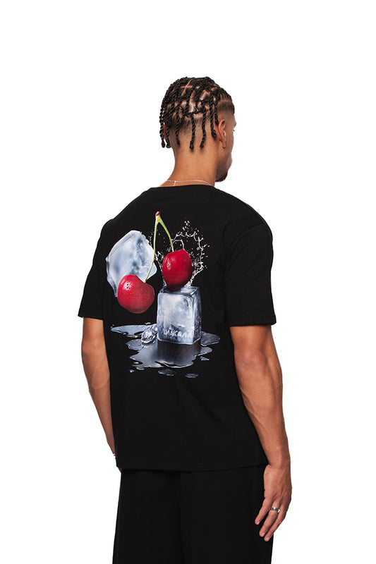 Mann trägt NC Tee Black Regular mit Neighbour's Cherries-Grafikdruck hinten, gesticktem OLAKALA-Logo auf der Brust; unisex, reguläre Passform.